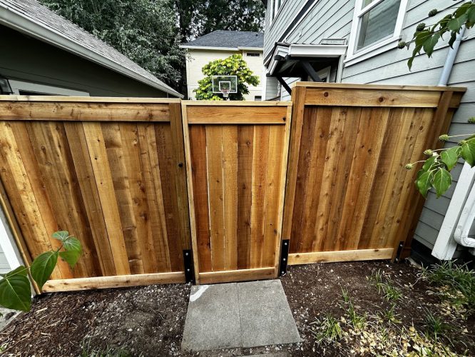Freshly painted wooden fence with gate in Chadderton by painters; walkway and basketball hoop behind. Pearl Painters not in Portland.