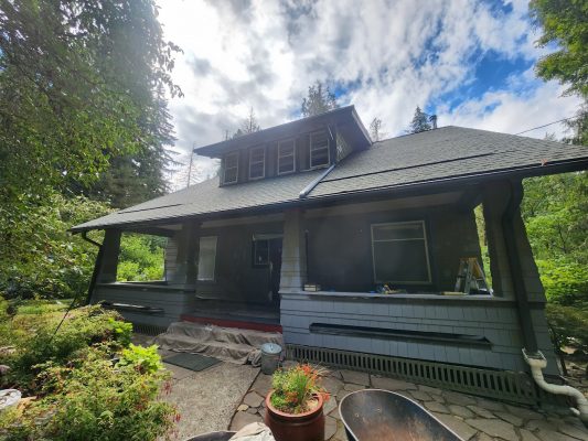 A two-story gray Gentry house in Portland with tarp and ladder by the porch, painted by Pearl Painters. Greenery surrounds it.