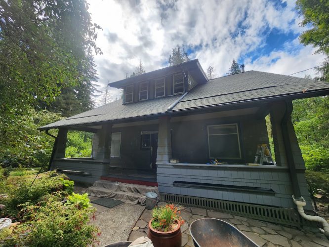 A two-story gray Gentry house in Portland with tarp and ladder by the porch, painted by Pearl Painters. Greenery surrounds it.