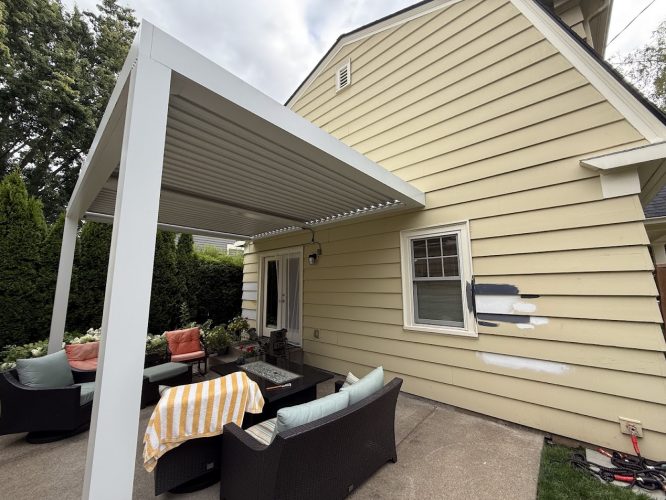 A painter tests paint swatches on a beige Portland home’s siding near a patio; Pearl Painters may paint it in August 2025.