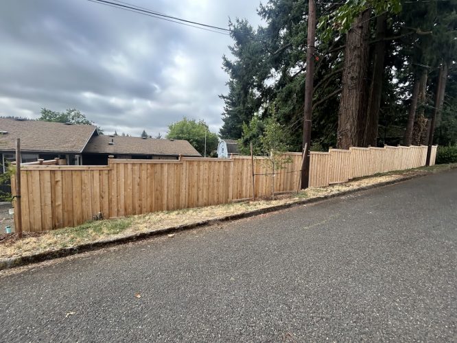 A new wooden fence on a sloped residential street in Portland, painted by Pearl Painters, houses and trees under cloudy skies.