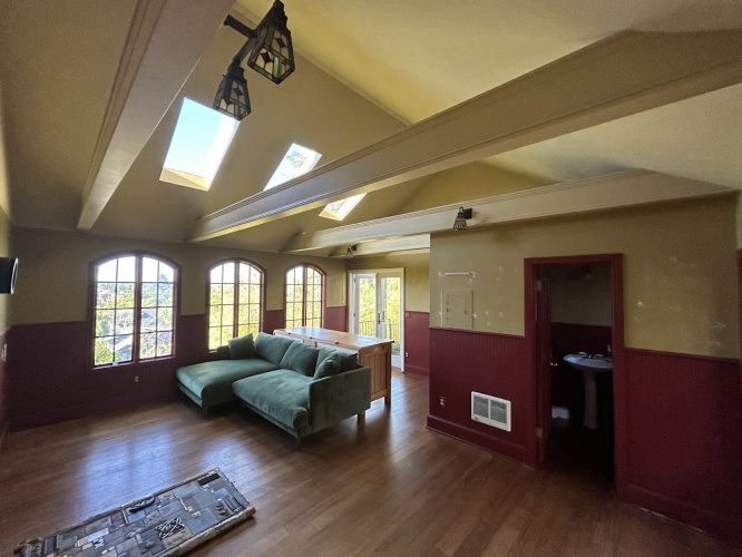 Room with wood floor, green sectional, skylights, arched windows, and open door to bathroom; painter work by Pearl Painters Portland.