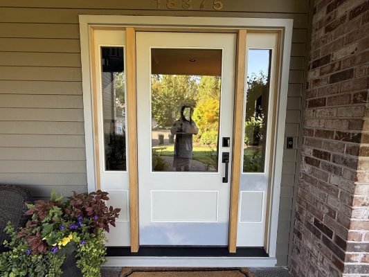 A white door with glass panels and wood trim is shown in sunlight; painter’s reflection visible. Painted by Pearl Painters, Portland.