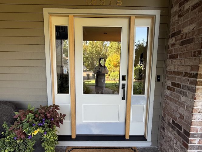 A white door with glass panels and wood trim is shown in sunlight; painter’s reflection visible. Painted by Pearl Painters, Portland.