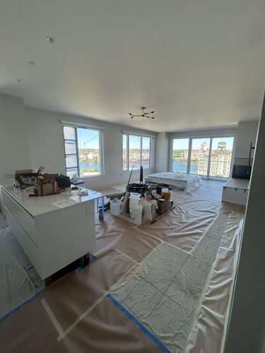 Apartment living room under renovation with covered floors and tools; city view. Painter activity by Pearl Painters, Allen, July 2025.