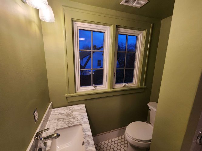 Interior bathroom painted green by Portland painter Duc of Pearl Painters. Features marble countertop, white toilet, hexagonal tile floor, and white-framed window. Suitable inspiration for an April 2025 refresh.