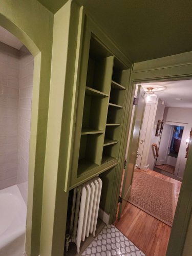 Painter Duc Interior created a vibrant green hallway in Portland with built-in shelves above a radiator, leading to a room with wood floors and part of a bathtub. Photo taken April 2025.