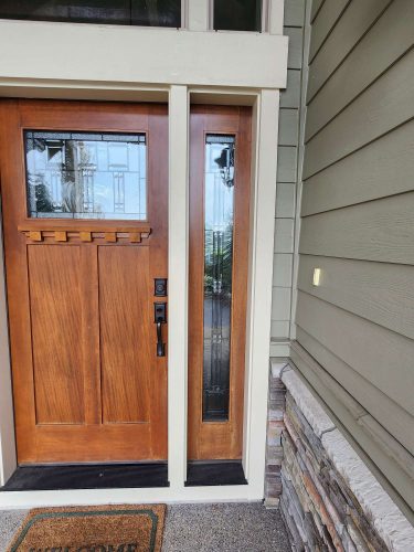 A Hansen wooden front door with a vertical glass panel, green siding, and stacked stone trim was painted by Pearl Painters, a painter in Portland.