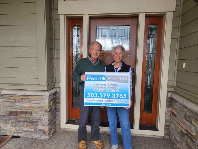 Two painters stand in front of a house door in Portland, holding a Pearl Painters sign advertising their exterior painting services and phone number for Hansen projects in April 2025.