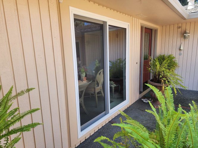 Photo by Ferlitsch, April 2025: Portland exterior shows a sliding glass door with white trim on beige siding near a red door, potted ferns, and outdoor reflections. Example of painting work by Pearl Painters.