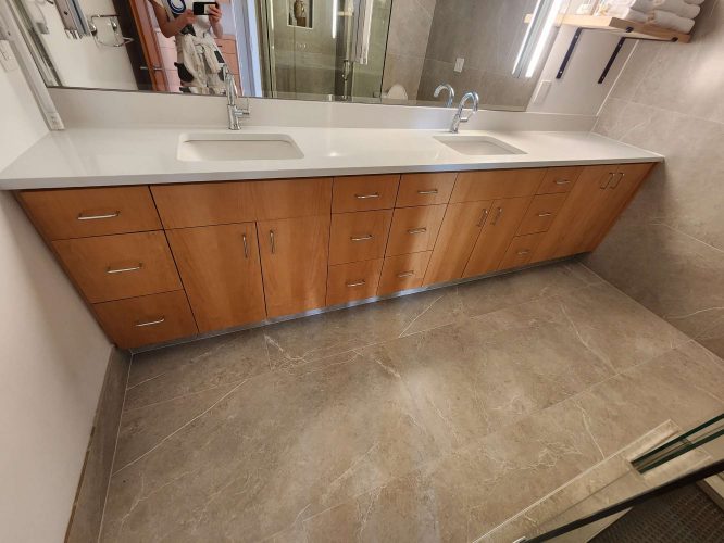 The Isadore double bathroom vanity includes wooden cabinets, a white countertop, two sinks, a large mirror, and beige marble floor tiles—ideal for a modern remodel. Pearl Painters in Portland can provide expert painting services for this upgrade.