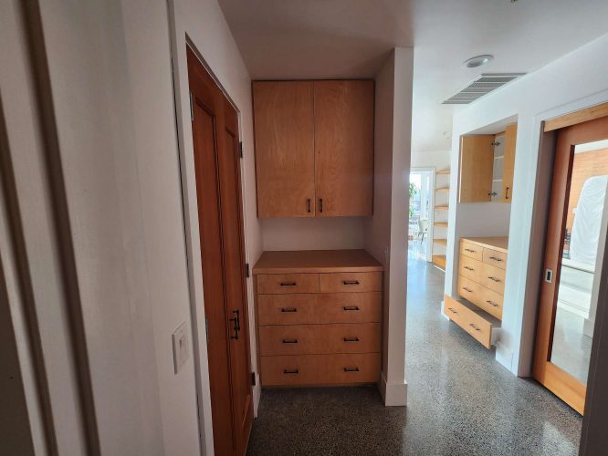 Hallway with built-in wooden cabinets and drawers, a closed wooden door on the left, and polished concrete floors. Cabinetry by Isadore, finished April 2025. Painter: Pearl Painters, Portland.