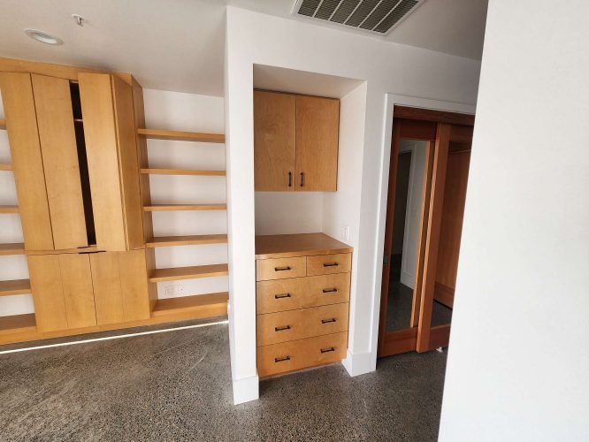 Isadore Cabinets are installed in a white wall with open shelves and a left-side cabinet, plus a tall glass door on the right. The polished concrete floor adds to the modern style. For painting needs in Portland, contact Pearl Painters.