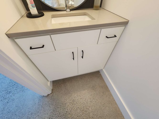 The Isadore white bathroom vanity, ideal for painting projects in Portland, includes two drawers, black-handled cabinets, and a gray countertop with built-in sink on a polished concrete floor. Pearl Painters recommends it for April 2025 updates.