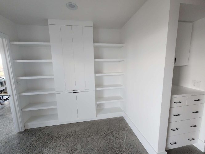 White Isadore built-in shelves and a central cabinet with closed doors are featured in a modern room with concrete flooring; additional cabinets and drawers are on the right. Painted by Pearl Painters, Portland.