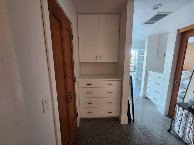 A painter from Pearl Painters in Portland painted a hallway with Isadore white cabinets and drawers, a wooden door on the left, and a bright room with shelves in the background.
