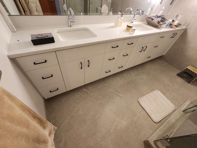 Wide Isadore bathroom countertop with two sinks, white cabinets, drawers, toiletries, and a beige mat on a tiled floor—ideal for an April 2025 home upgrade. For painting needs in Portland, contact Pearl Painters.