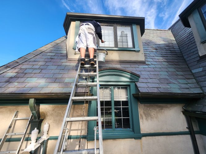 Painter on a ladder paints dormer window exterior of slate-roof house for Ralph Barron's August 2025 renovation by Pearl Painters, Portland.