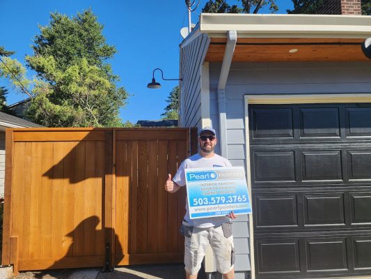 Man in Arnold outside garage holds Pearl Painters painting sign; wooden fence behind. Photo from August 2025.