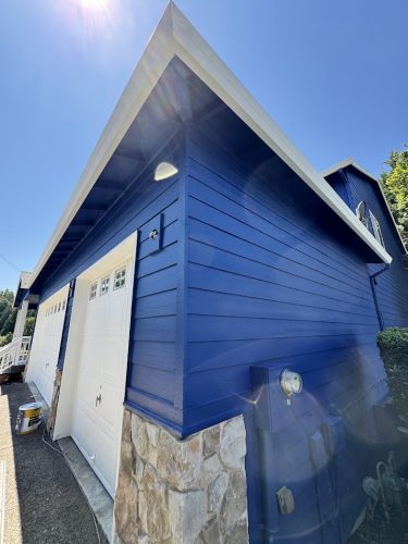Jennings garage painted bright blue by Pearl Painters, with white door and stone accents, Portland, July 2025.