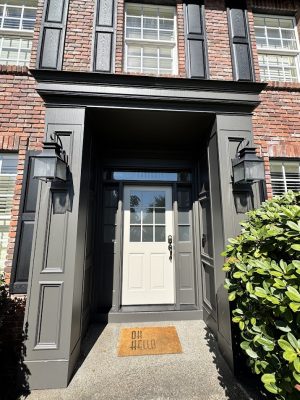 Brick house front entrance with gray door, black trim; painted by Pearl Painters, Portland. Shrubs and "OH HELLO" doormat visible.