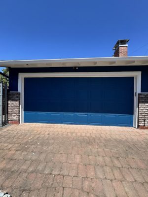 A blue garage door and brick driveway at a blue and brick house; painted by Pearl Painters in Portland, July 2025.