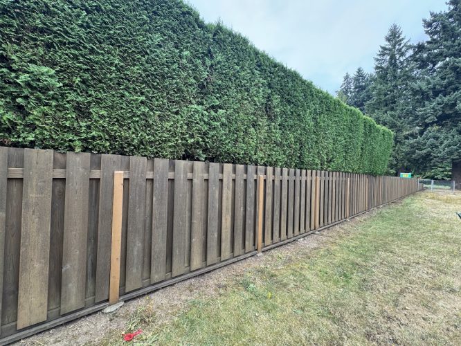 A Craytor exterior in Portland shows a wooden fence by a hedge; grass, trees, and clouds are visible. Painted by Pearl Painters.