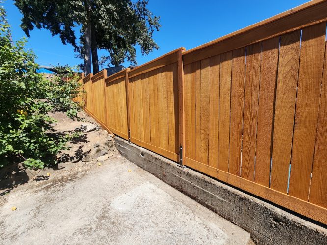New wooden fence in Arnold along a sloped yard, with plants and concrete base, ready for painting by Pearl Painters.
