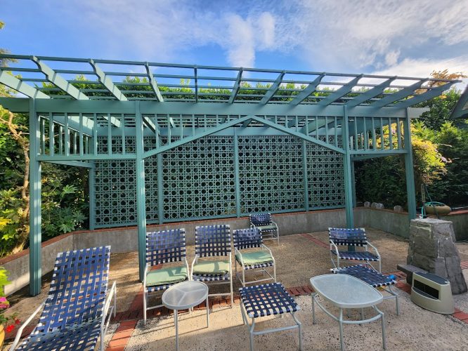 Outdoor patio with blue and white chairs, round tables, pergola, and patterned wall; styled like a painting in Portland.
