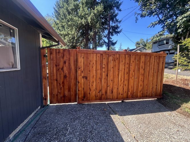 A wooden privacy fence and gate by a house and driveway in Portland, painted by Pearl Painters under a clear sky.