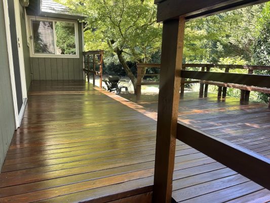 A painter from Pearl Painters stained a wood deck in Pitney; railings and trees visible on a sunny August 2025 day.