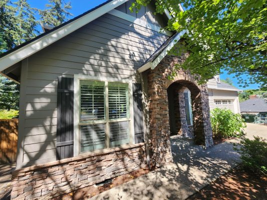 A Holley house with gray siding and stone accents painted by Pearl Painters, Portland, in sunlight with tree shadows.