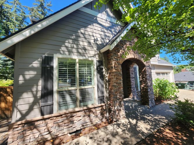 A Holley house with gray siding and stone accents painted by Pearl Painters, Portland, in sunlight with tree shadows.