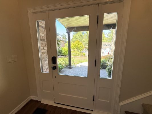 White front door with side glass panels, seen from inside a Portland home, painted by Pearl Painters; porch and greenery outside.