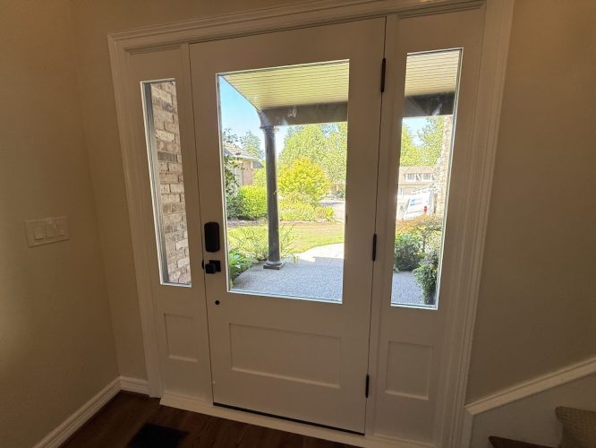 White front door with side glass panels, seen from inside a Portland home, painted by Pearl Painters; porch and greenery outside.