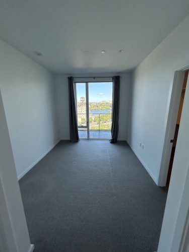 Empty carpeted room in Allen with white walls—good for painting. Large window, glass door to balcony, gray curtains at sides.