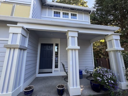 A modern two-story Anderson house in Portland with a blue door, porch, plants, and chairs; painted by Pearl Painters.