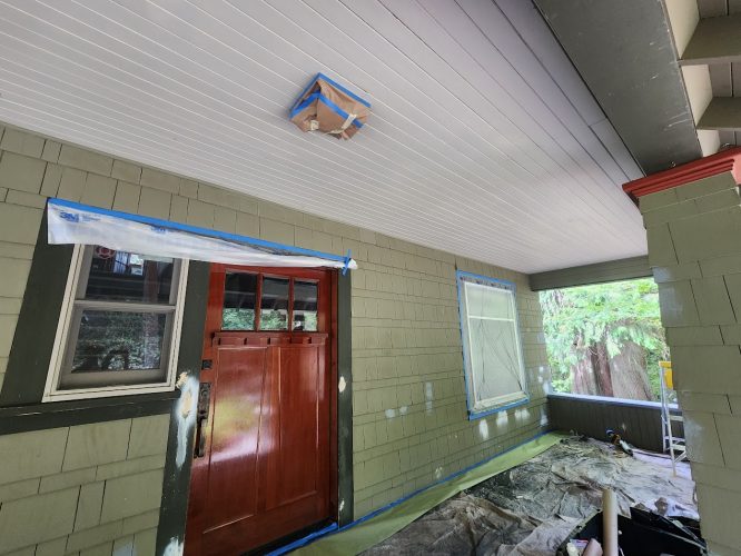 Portland porch prepped for painting by Pearl Painters: red door, green siding, taped windows, drop cloths on floor.