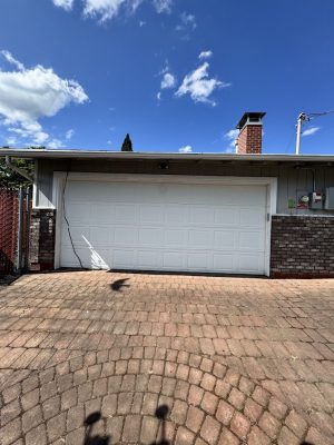 A white Deppe garage door on brick paving with brick and wood siding, painted by Pearl Painters in Portland, July 2025.