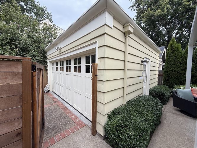 Beige detached garage with white door and bushes in Portland, prepped for painting by Pearl Painters for Johnson project.