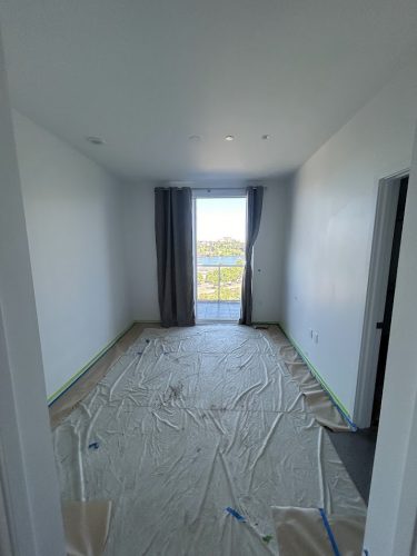 Empty room with white walls, plastic-covered floor for painting prep. Photo by Pearl Painters in Allen, July 2025.