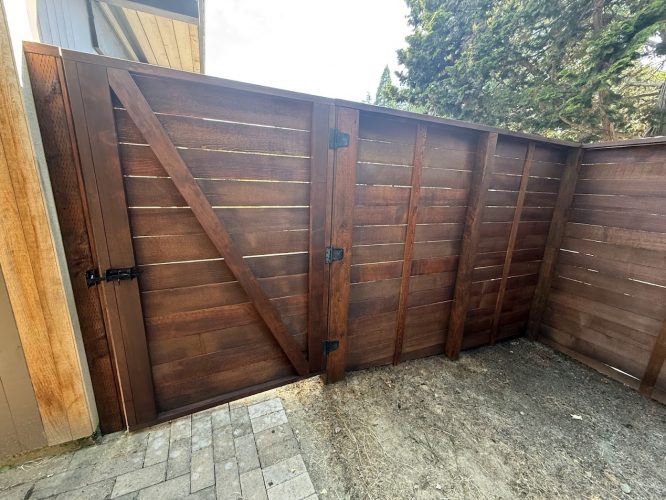 A Portland painter inspects a wooden fence and gate with horizontal slats in Harvey, July 2025, for Pearl Painters.