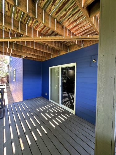 Painted blue siding, sliding glass door, and covered wooden deck with sunlit shadows. Painted by Pearl Painters in Portland.