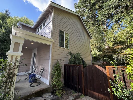 A tan two-story house in Portland with porch, chairs, and gate, freshly painted by Pearl Painters in August 2025.
