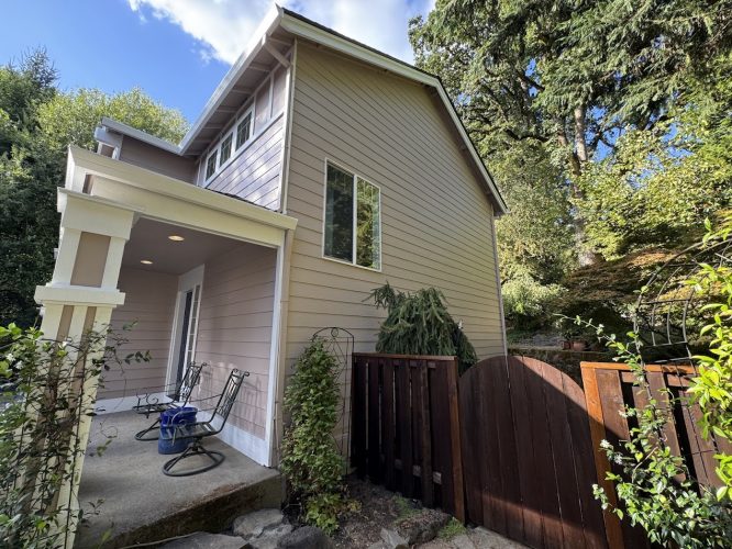 A tan two-story house in Portland with porch, chairs, and gate, freshly painted by Pearl Painters in August 2025.