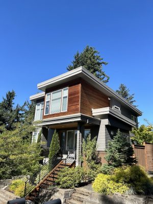 Painted by Pearl Painters, this modern two-story Portland home features wood and gray siding, large windows, and greenery.