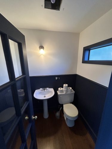 Small bathroom in Portland with dark blue painted walls and door by Pearl Painters; wood floor, pedestal sink, and wall light.