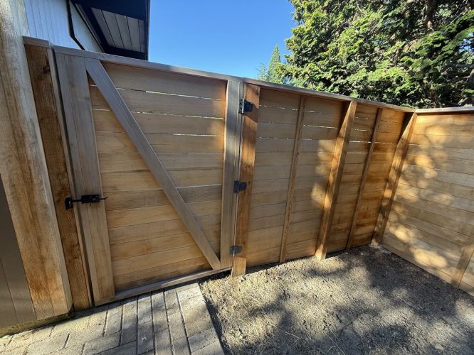 A wooden privacy fence with a gate by Harvey, painted by Pearl Painters, separates two Portland yard areas.