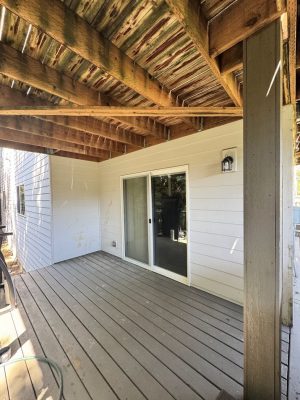 Covered wooden deck with sliding glass door, white siding, and exposed beams painted by Pearl Painters in Portland.
