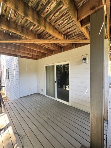 Covered wooden deck with sliding glass door, white siding, and exposed beams painted by Pearl Painters in Portland.